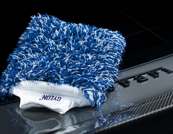 A blue-white wash mitt from GYEON rests on a Ferrari badge.