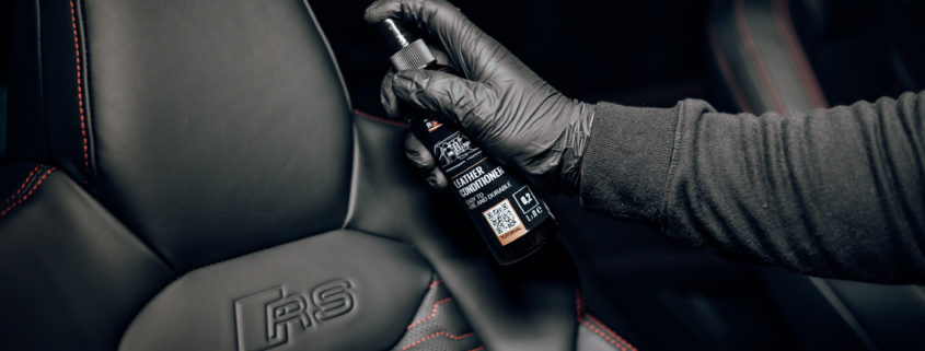 A gloved hand sprays ADBL Leather Care onto a black leather seat.
