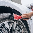 Maxshine Soft Grip Tyre Cleaning Brush - Short Handle Maxshine short-handle tyre cleaning brush being used to scrub a car tyre beside a silver alloy wheel covered in cleaning foam.